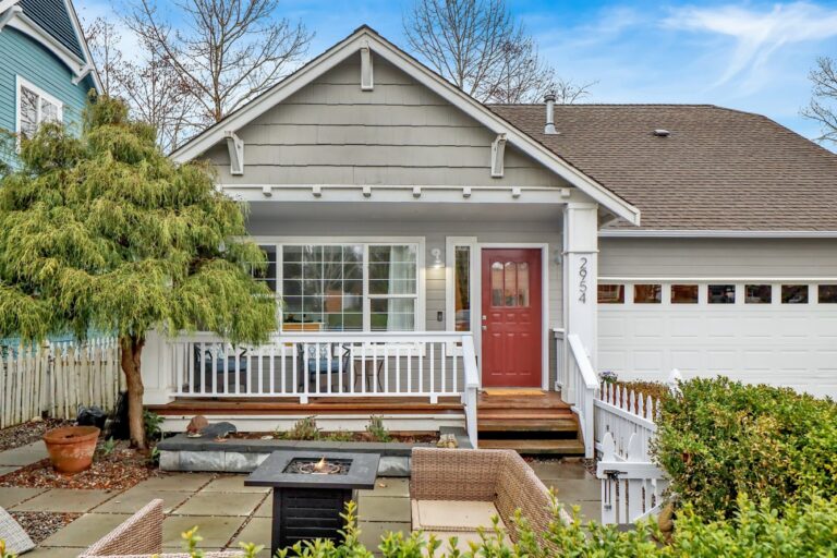 Gray house with a red front door, covered porch and landscaped front yard.