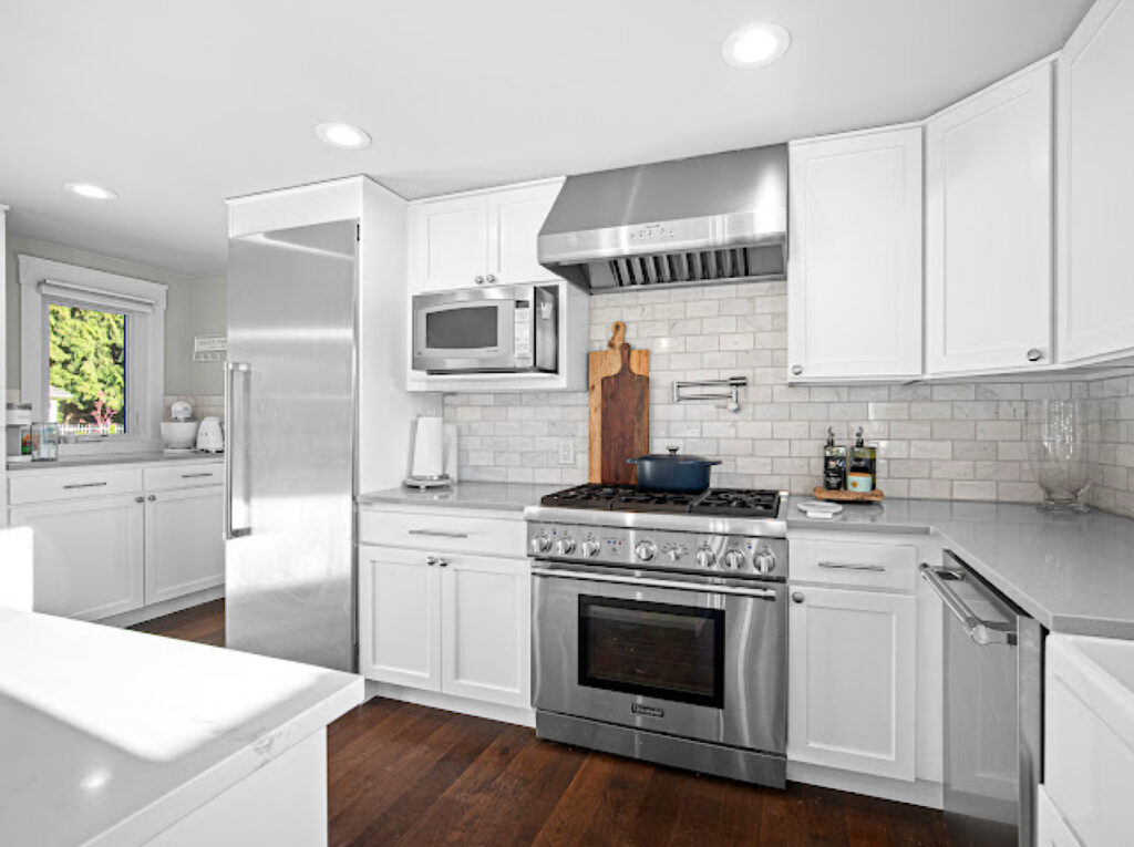 White kitchen with stainless steel appliances, tiled backsplash and wood flooring.
