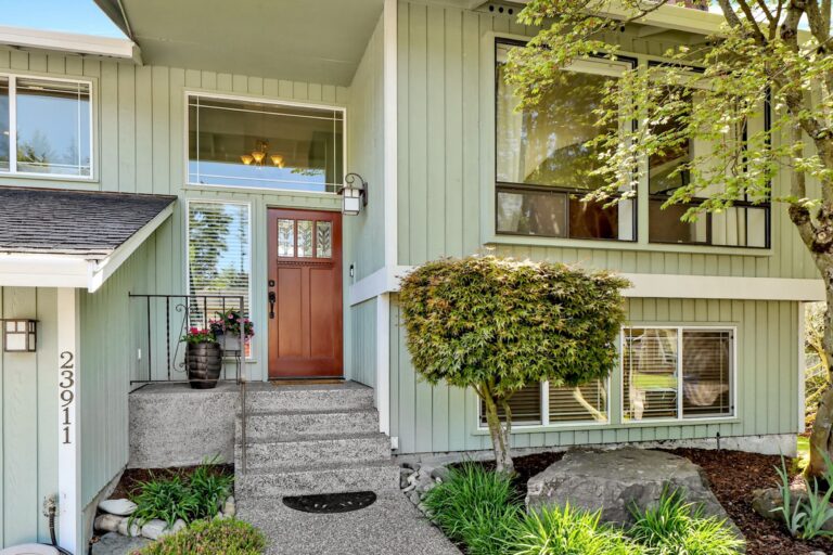 Covered home entry with a red front door, concrete steps and garden plants.