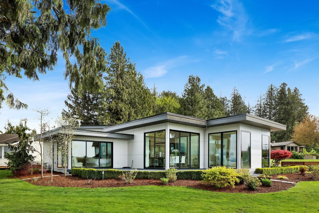 Single story white home with tall windows, a lawn and landscaped garden beds.