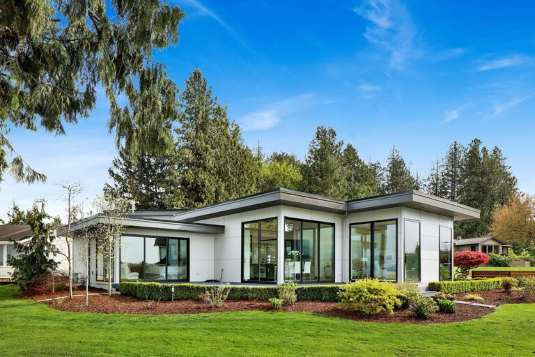 Single story white home with tall windows, a lawn and landscaped garden beds.