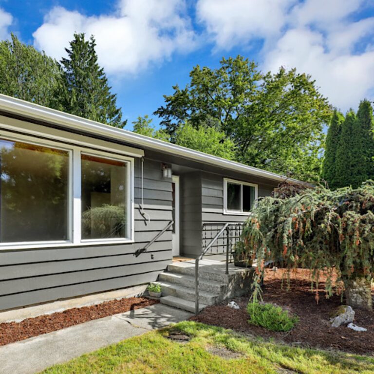 Gray home with large windows, a front walkway and garden plants.